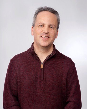 Portrait of a smiling man in a maroon sweater against a light grey studio backdrop.